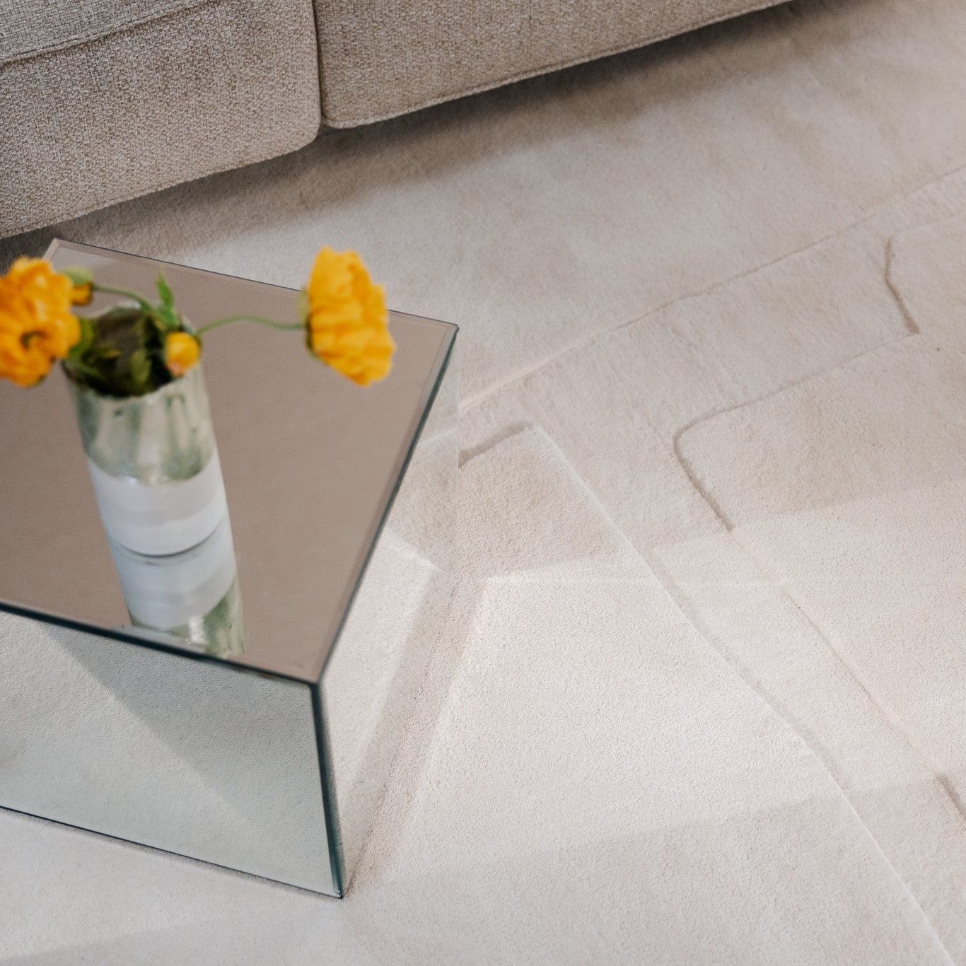 Acoustic decor with soft beige rug, mirrored glass table and yellow flowers beside a neutral sofa