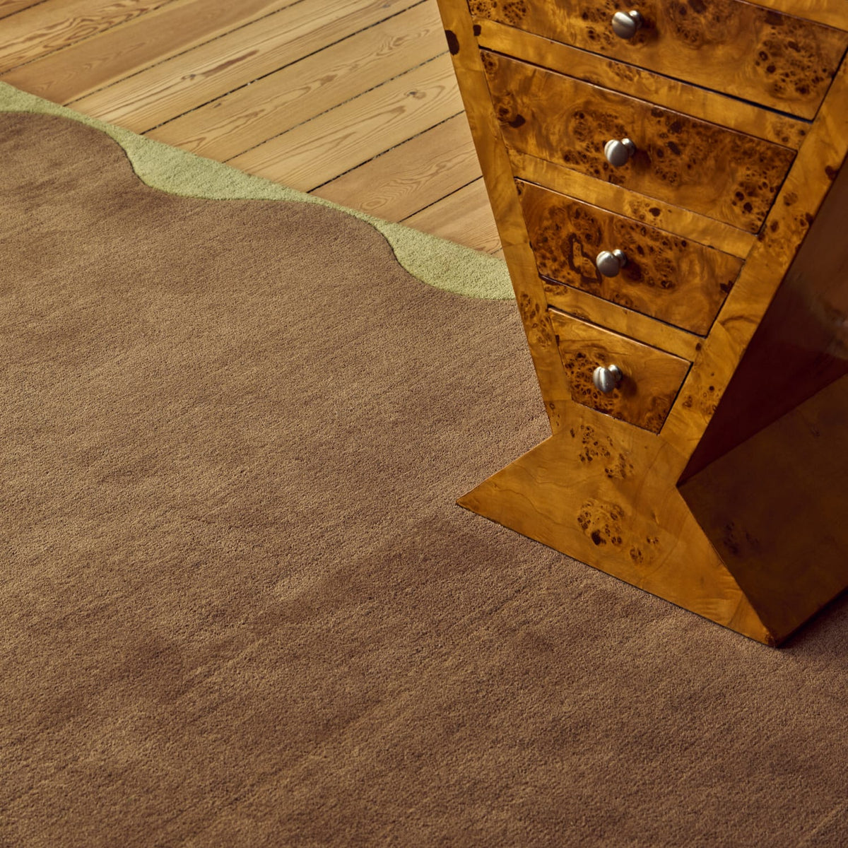 A close-up of a brown textured area rug in a room setting, shown next to a wooden furniture piece with silver knobs.