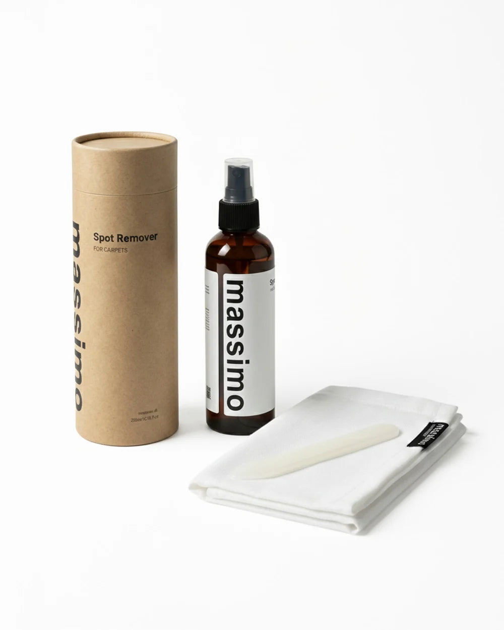 Massimo Spot Remover kit featuring an amber spray bottle, a brown kraft paper tube, and a folded white cloth with a spatula tool, set against a plain white background.